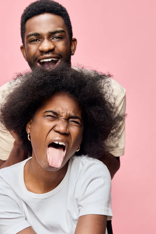 Fun and joyful young couple displaying strong emotions with playful expressions on a pink background, showcasing happiness and togetherness