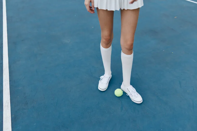 Young woman in tennis attire standing on a court, featuring white socks and shoes, showcasing a confident pose and joyful emotion, ideal for sports marketing