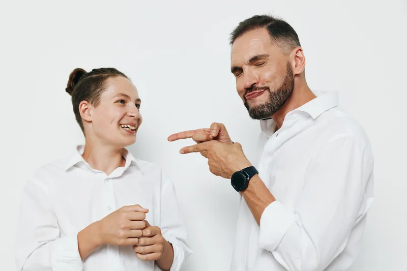 A professional man in business attire shares a warm smile with a younger colleague against a clean, isolated colored background, conveying positivity, confidence, and collaborative emotion in a