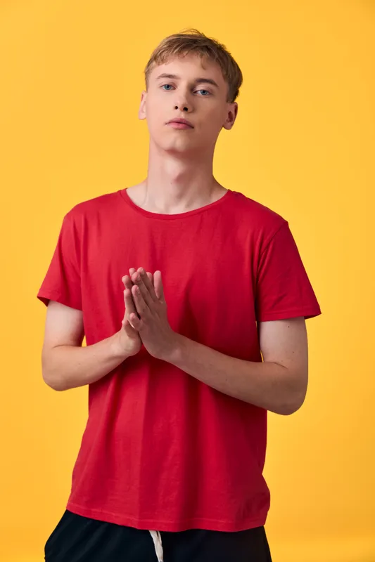 Hands in prayer gesture, man in red shirt against yellow background, calm expression and pose, minimalism studio setup for wellness, lifestyle, motivation themes