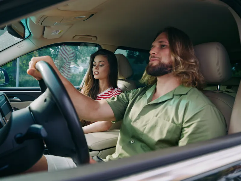 Two adults sit inside a car, with a focused driver at the wheel and a curious passenger beside, capturing a candid moment of travel and daily commute.