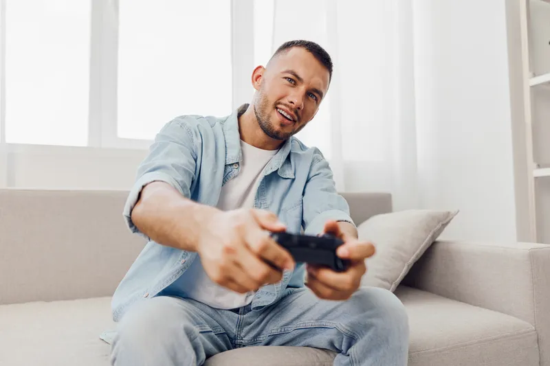 Engaged man playing video games at home, showcasing the blend of relaxation and technology, while embracing moments of authentic imperfection and emotional minimalism.