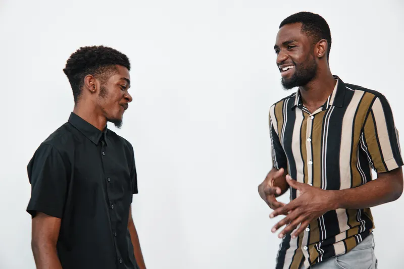 Two young black men with dark skin smiling and talking together in casual clothes on white background. Friendship, communication and positive interaction between friends.