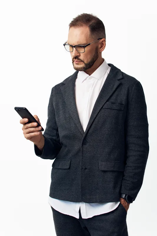 A professional man in a tailored suit stands against an isolated colorful background, focused on a mobile device, expressing calm, confident, and thoughtful business emotions.