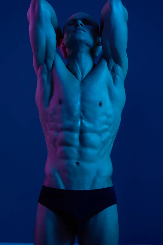 Athletic man posing with strong physique under dramatic blue lighting, showcasing a powerful silhouette and intense emotion. Perfect for fitness and wellness themes.