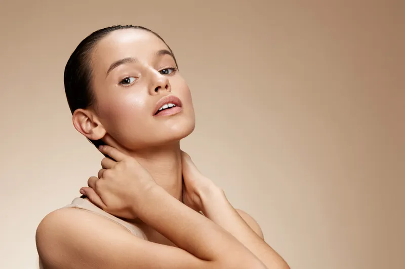 A young model with a natural complexion poses softly against a warm beige background, exuding confidence and serenity, embodying beauty and wellness