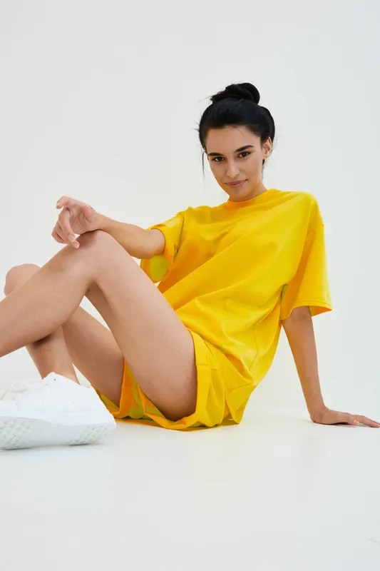 young woman in yellow casual outfit sitting on floor with white sneakers, relaxed pose, minimalist white background, natural expression, modern style