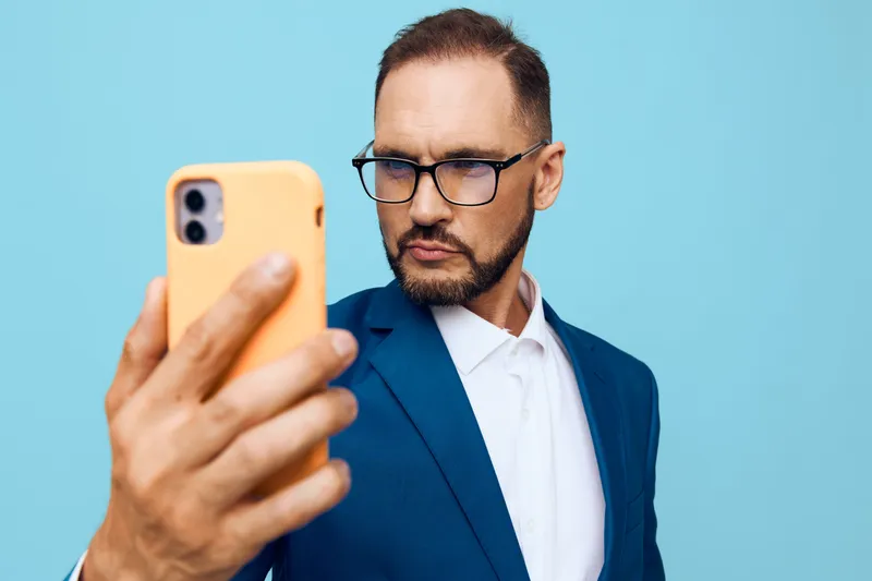 A focused business professional poses for a self portrait against a solid colored backdrop, conveying confidence, concentration, determination, and a ready mindset for strategic work.