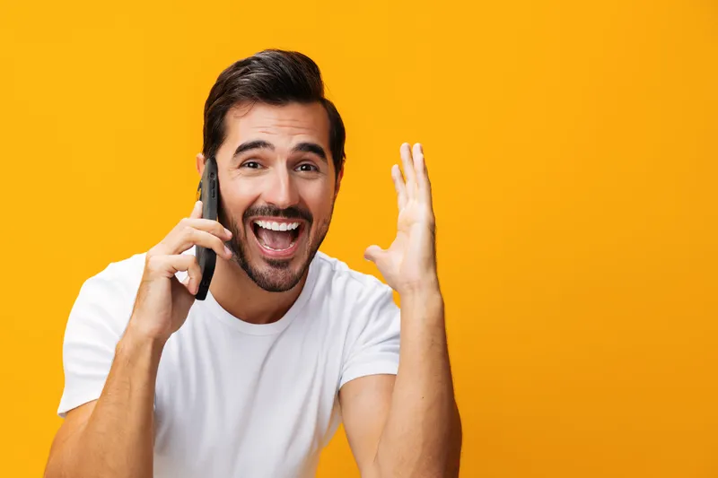 Мужчина в очках, с желтым смартфоном, счастливо улыбается, показывая зубы