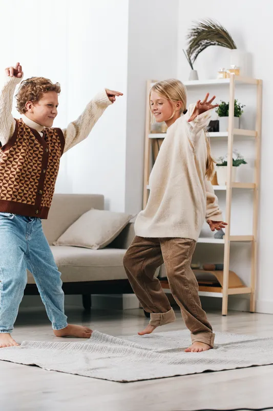 Two children dance playfully in a bright living room, their joyful movement framed by a cozy rug, soft furniture, and warm natural light that captures carefree energy.