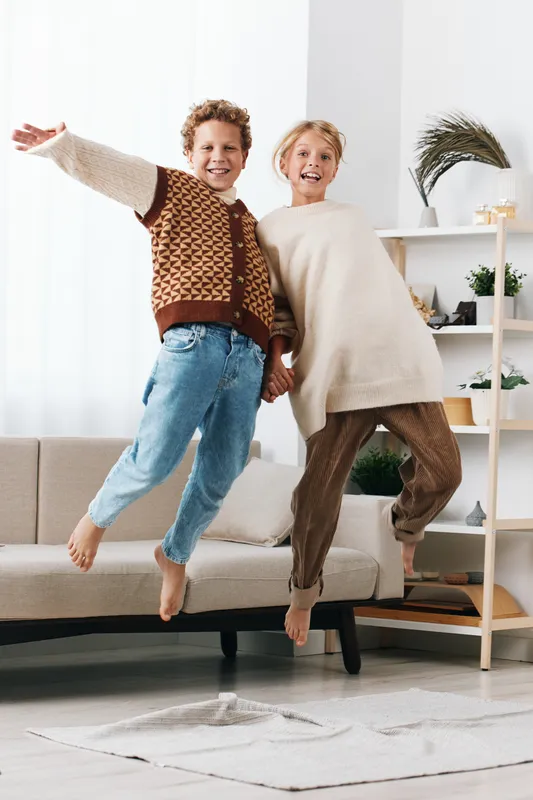 Authentic moment of children at play, two kids jumping with joy indoors, capturing candid lifestyle and playful school vibes in a cozy home setting.