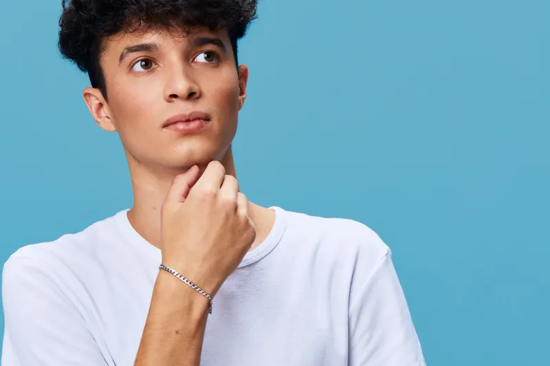 thoughtful man wearing white shirt touching chin on blue background, young casual style, curious expression, studio portrait photography
