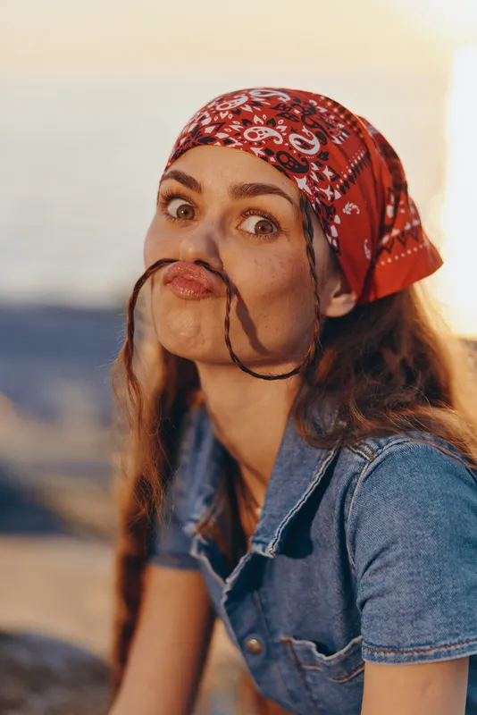 Lifestyle woman in modern boho-western denim street style with a red bandana, playful expression, and film color tones capturing fun and carefree vibes outdoors.