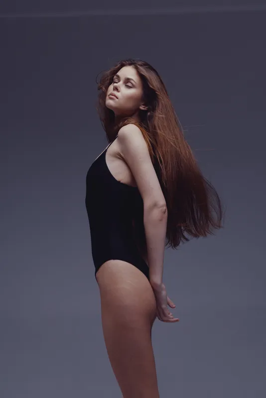 slender woman posing in black bodysuit with long hair against dark background, elegance, fashion, beauty