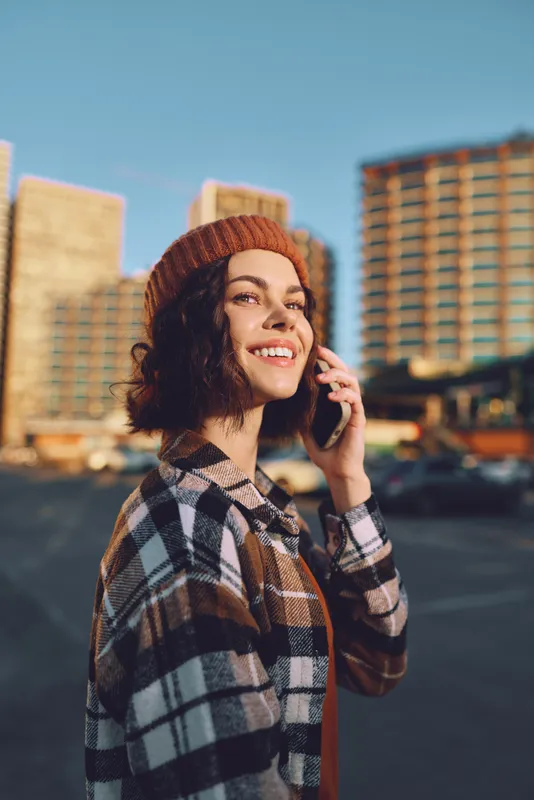 woman smile phone urban beanie candid lifestyle golden hour portrait of a joyful young woman talking on mobile in city street, authenticity, golden hour glow and mindful living mood.