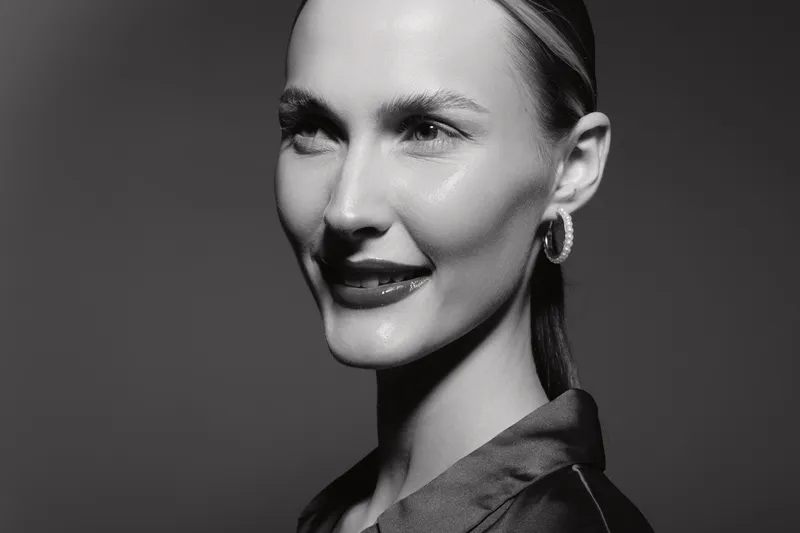Portrait of a smiling Caucasian woman with fair skin and blonde hair in studio, wearing earrings and a dark blouse. Concept for beauty and elegance.