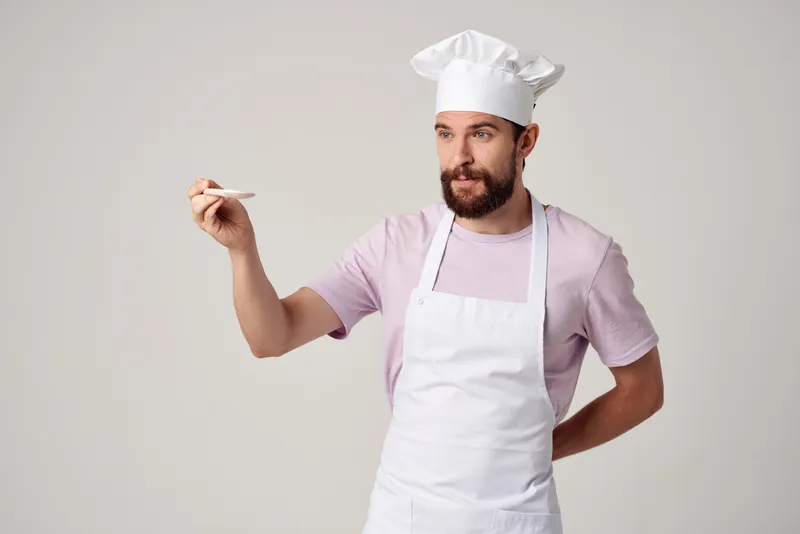 Шеф-повар в униформе работает с кухонной утварью, занимаясь приготовлением пищи
