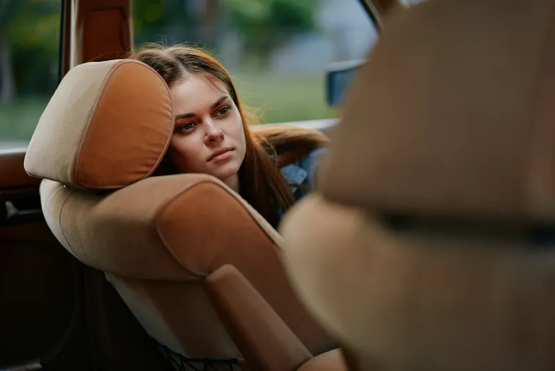 Pensive young woman resting her head on a car seat, reflecting on her thoughts in a soft, natural light setting, showcasing emotions of contemplation and tranquility.