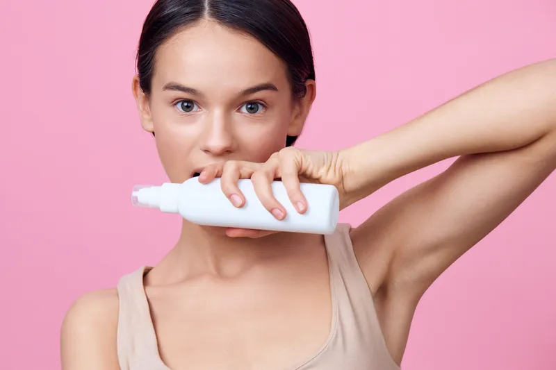 Young woman holding a white cosmetic bottle near her face, showcasing gentle skincare on a pink background, emphasizing beauty and self care concepts