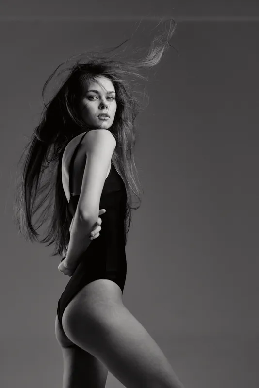 Black and white artistic portrait of a woman in bodywear with flowing hair and expressive pose.