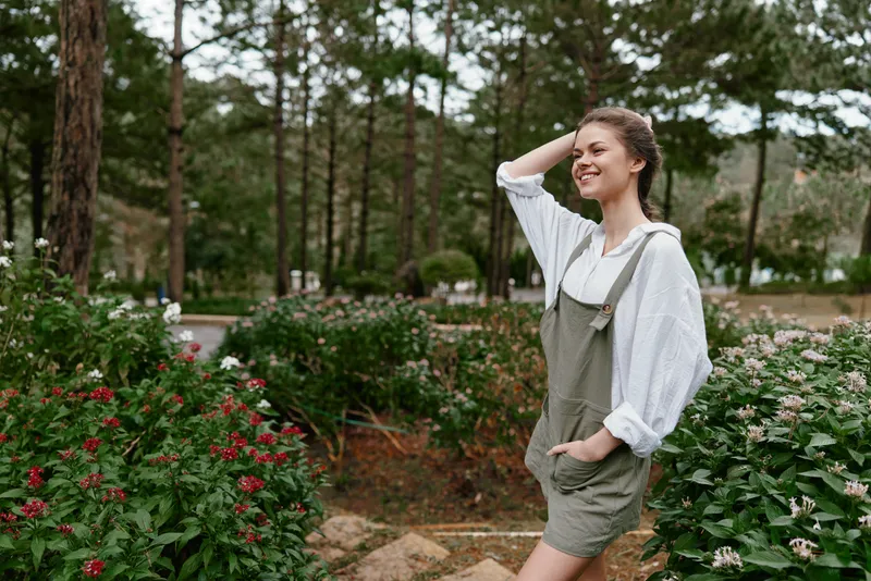 Young woman enjoying nature in a lush green garden, exuding happiness in casual attire during spring, surrounded by vibrant flowers and trees