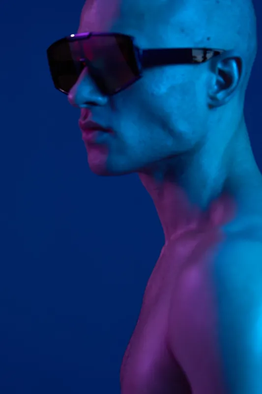 Stylish man with sunglasses poses confidently against a vibrant blue background, showcasing modern fashion and striking contrast in light. A unique portrait.