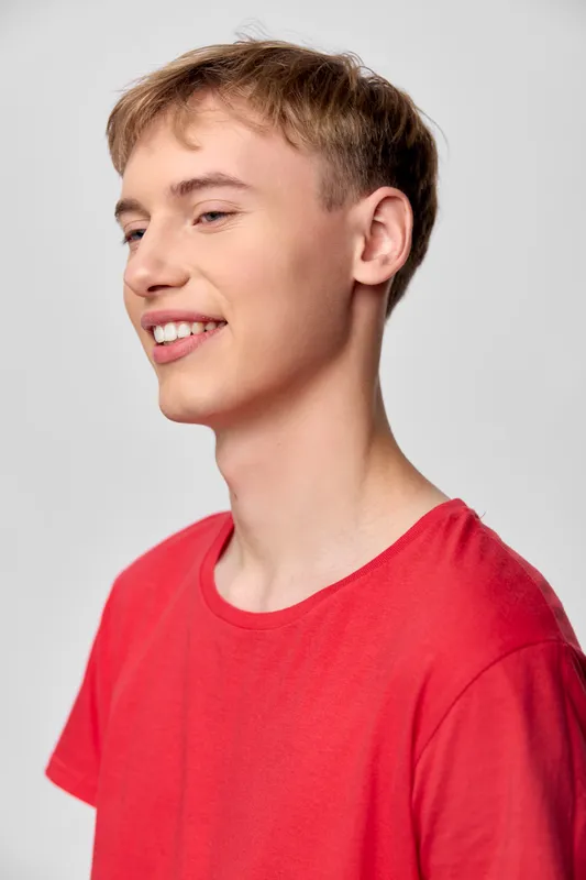 Young man in a red casual shirt with a bright smile in a studio setting, relaxed and confident, showcasing everyday fashion and approachable vibe for lifestyle and headshot style