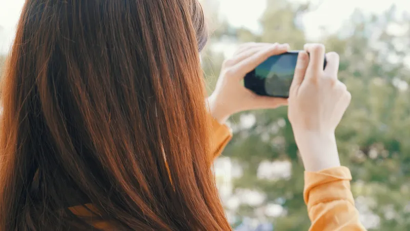 Женщина с телефоном в руке фотографирует природу на камеру во время отпуска, на заднем плане пейзаж