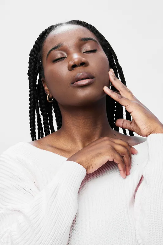 Calm African woman with braids, closed eyes, and a serene expression wearing a light sweater against a minimalistic background Relaxation, beauty, and self care concept