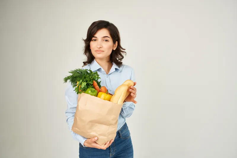 Брюнетка с пакетом продуктов из супермаркета: здоровая еда, овощи