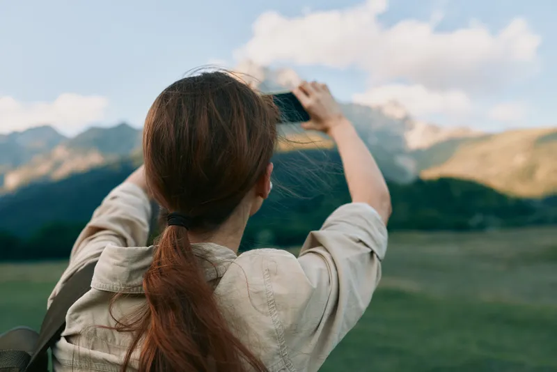 Woman outdoors photographs mountains with a camera, showcasing lifestyle photography in a natural landscape, peaceful adventurous mood, focus on exploration and scenery