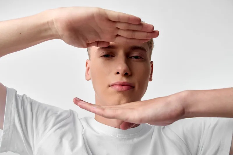 Hands framing face in a clean studio with soft lighting and white tee, minimal composition, focus on framing and balance for photography, conceptual stock shot