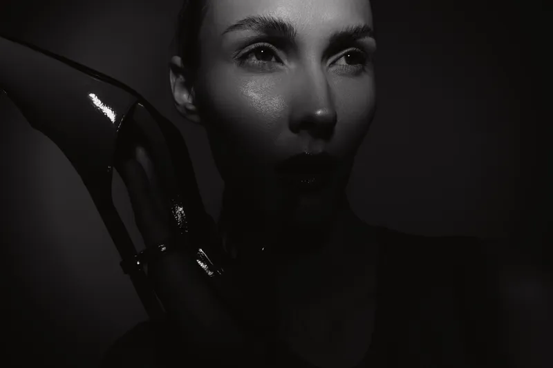 Closeup of a young Caucasian woman with pale skin and wet glossy hand in dark moody lighting, concept of beauty and mystery.