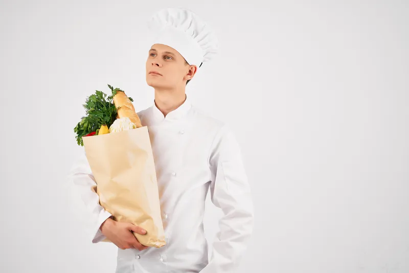 Мужчина в поварской форме с упаковкой продуктов жестикулирует рукой на кухне, пропагандируя здоровое питание