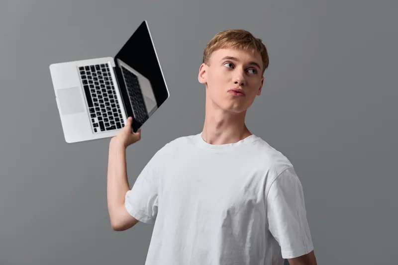 Man in a white shirt tossing a laptop in the air, highlighting technology and creativity in a dynamic studio, depicting thinking, innovation and modern work culture