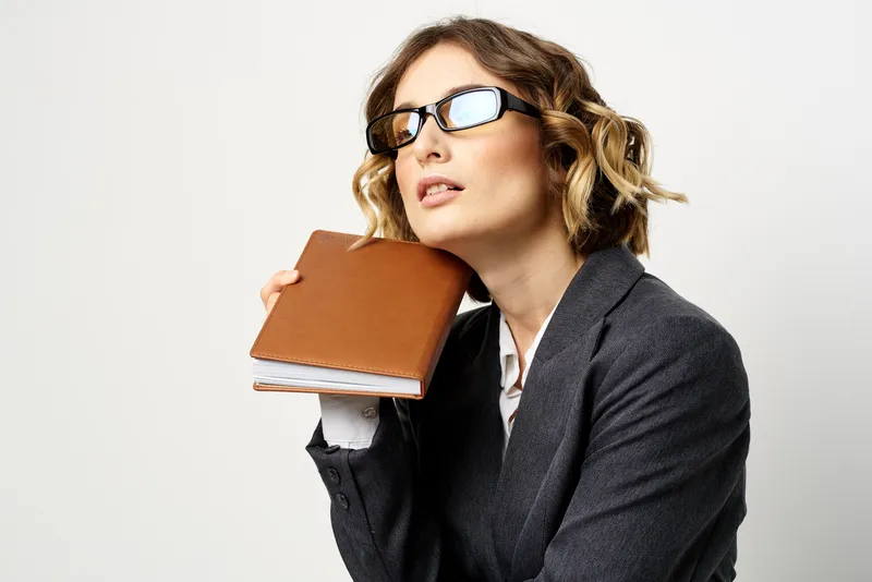 Женщина на работе с книгой в руке на светлом фоне, в классическом костюме и очках, изображение головы