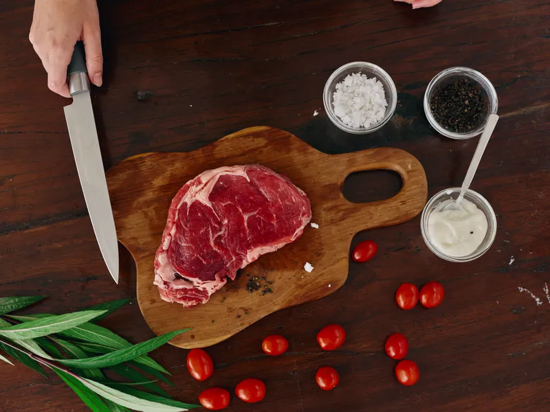 Женщина с ножом в руке нарезает свежее мясо стейка для жарки на кухне