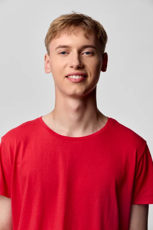 Smiling man in a red t shirt stands against a neutral backdrop, relaxed pose and confident expression, bright casual look suitable for lifestyle stock photography and fashion themes for advertising