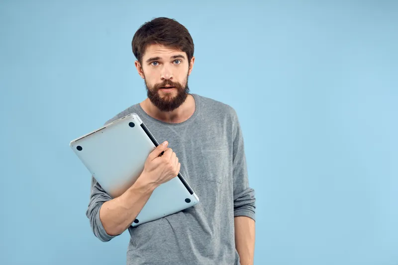 Бородатый мужчина с ноутбуком в руках, беспроводные технологии, эмоции, синий фон