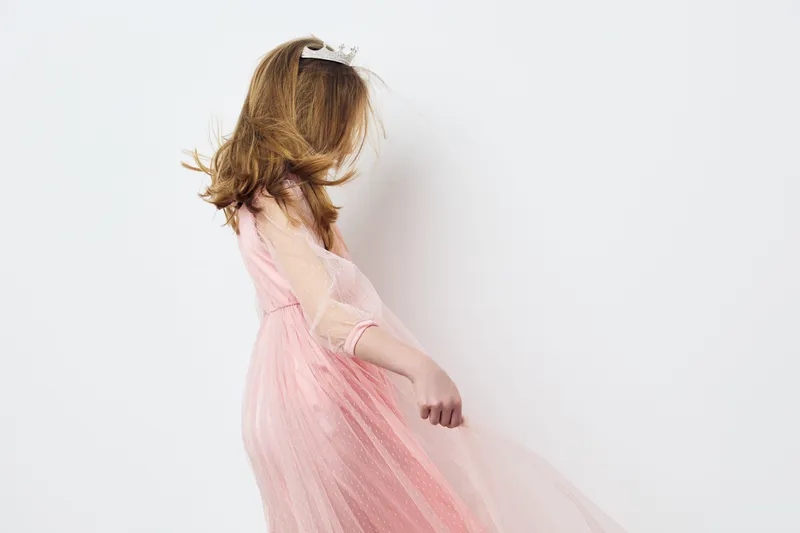Young girl in a pink tulle dress twirling gracefully, showcasing joy and elegance against a minimalist white background, embodying a feeling of childhood innocence