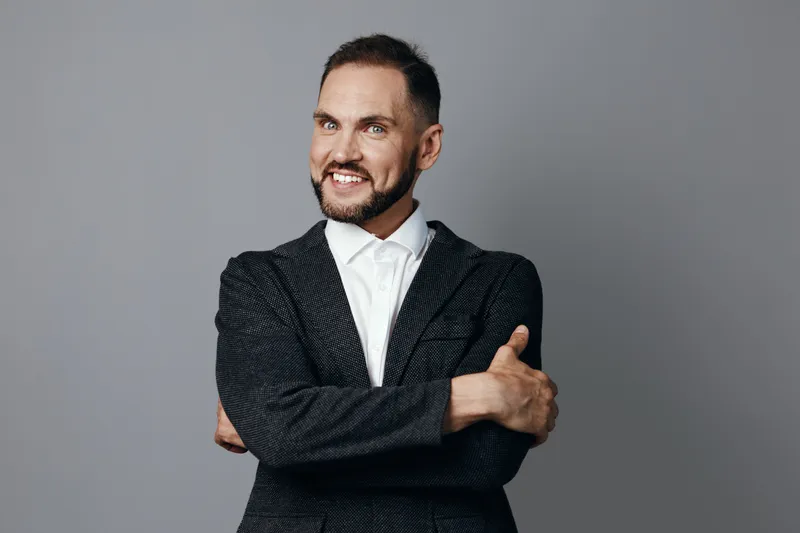 Professional man in a dark blazer stands with arms crossed and a warm smile, conveying confidence, focus, and approachability against an isolated colored background.