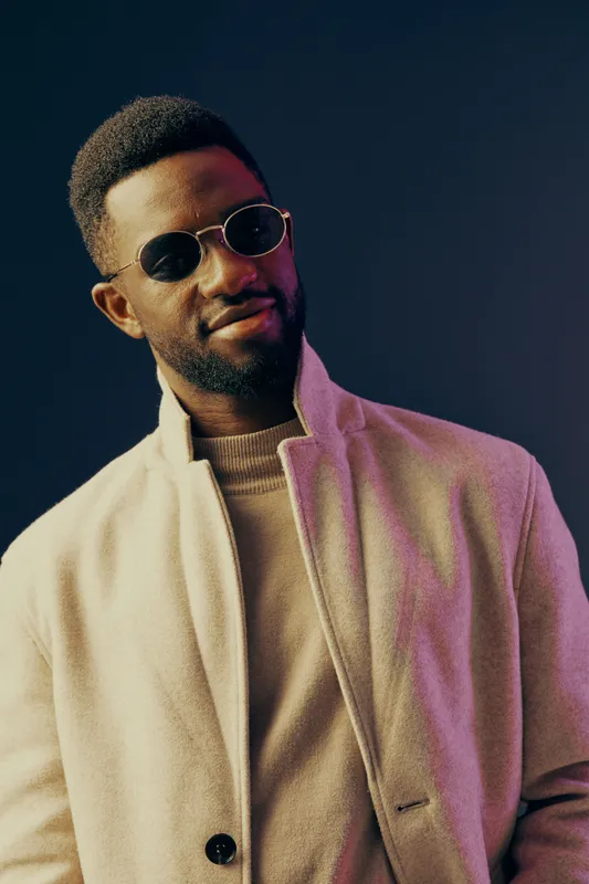 Stylish young man with sunglasses in a cozy light jacket, showcasing confidence against a deep blue background Fashion, casual style, confidence, modern aesthetics, and urban vibe