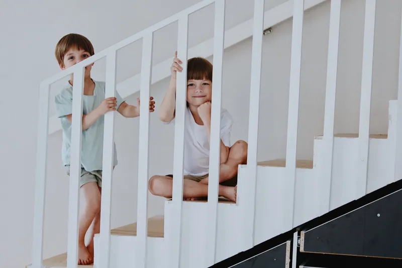 Two cheerful boys playing on a staircase, captured in a bright and spacious interior. Their playful nature brings joy to the scene in this lively home atmosphere.