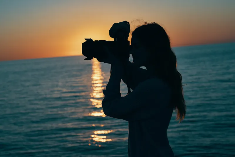 Женщина-фотограф с камерой на закате у моря на фоне природного пейзажа
