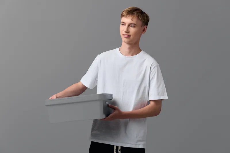 Man in a white t shirt holding a gray box, ready for delivery or shipment, minimalist studio setup, packaging and handover scene, the image conveys logistics and order fulfillment in a clean style