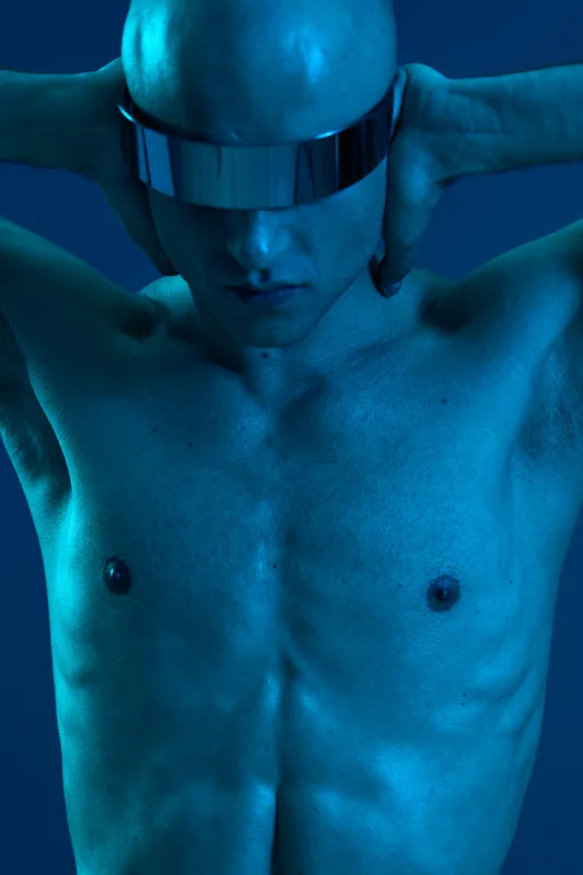 Artistic portrait of a man in futuristic glasses, showcasing a striking blue light and a dramatic pose. The image emphasizes a modern and bold aesthetic.