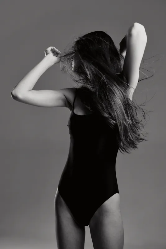 Black and white artistic woman in black bodysuit posing with hair covering face.