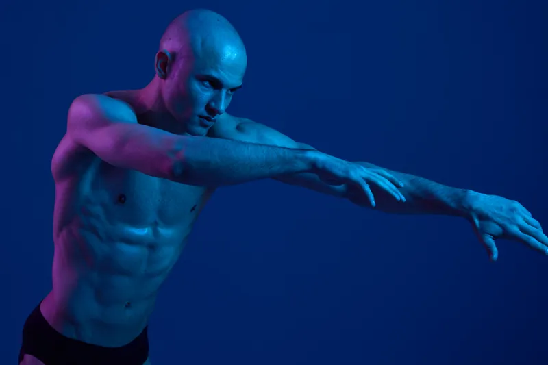 Athletic man posing with dynamic movements against a vibrant blue background, showcasing strength and grace in an artistic expression.