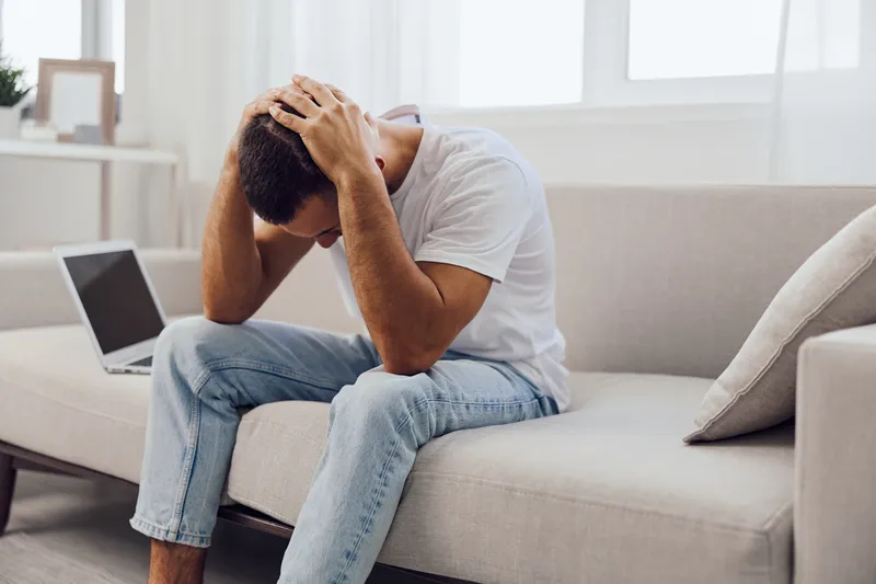 Frustrated man struggles with AI anxiety while sitting on a couch, emphasizing the blend of personal and work challenges in modern life.
