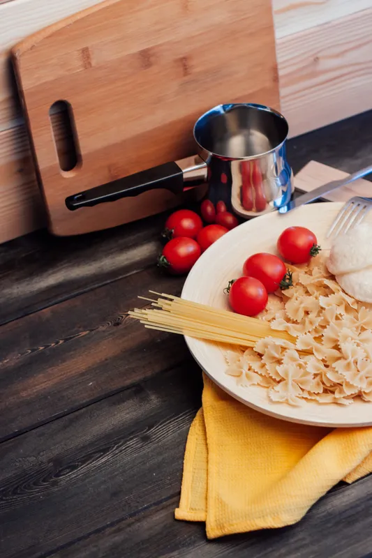 Итальянская паста с помидорами черри, приготовление еды на кухне, деревянный стол
